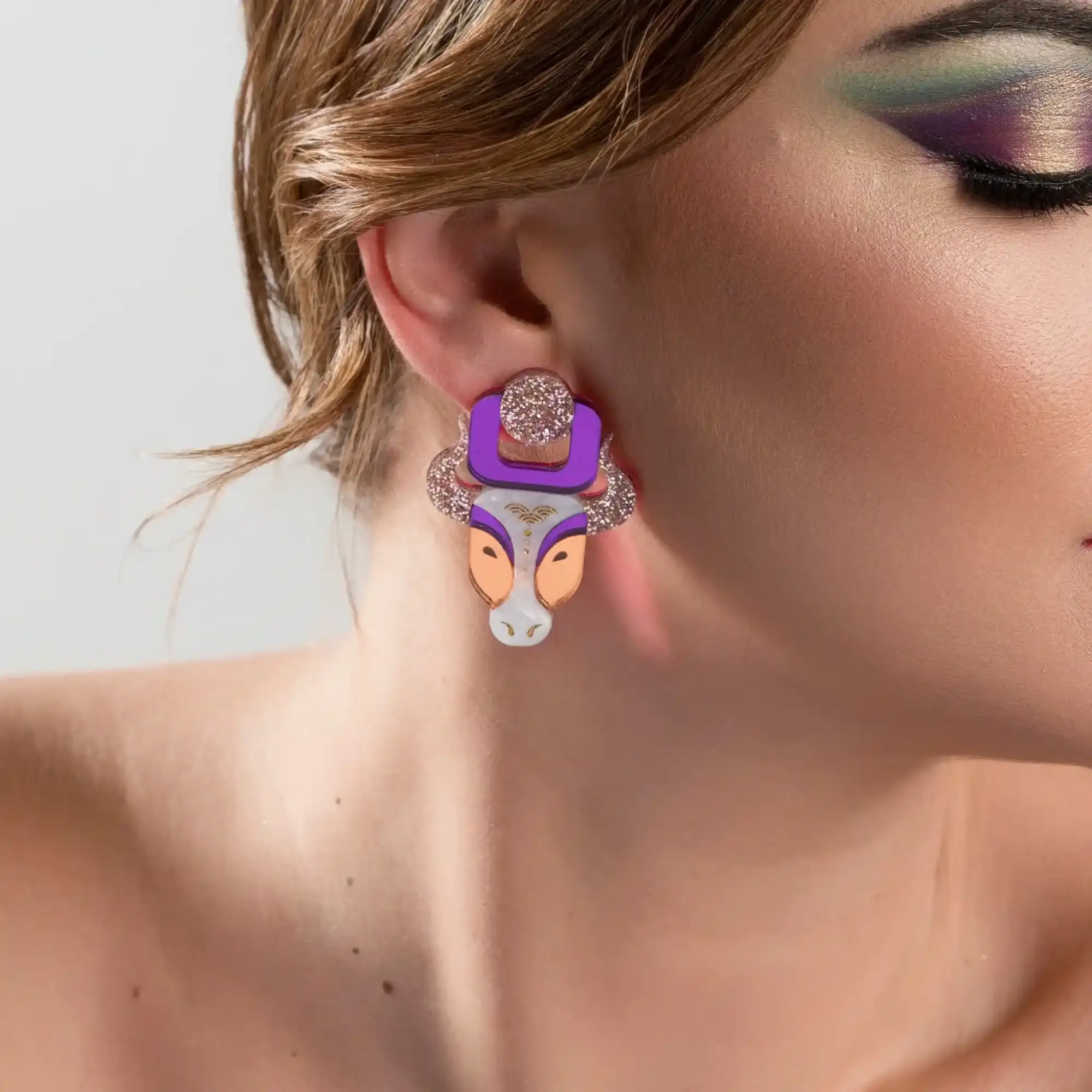 Modelo luciendo los pendientes Vaca Sagrada India, con diseño en metacrilato espejo, detalles de glitter y nácar pintados a mano, perfectos para un look llamativo y elegante