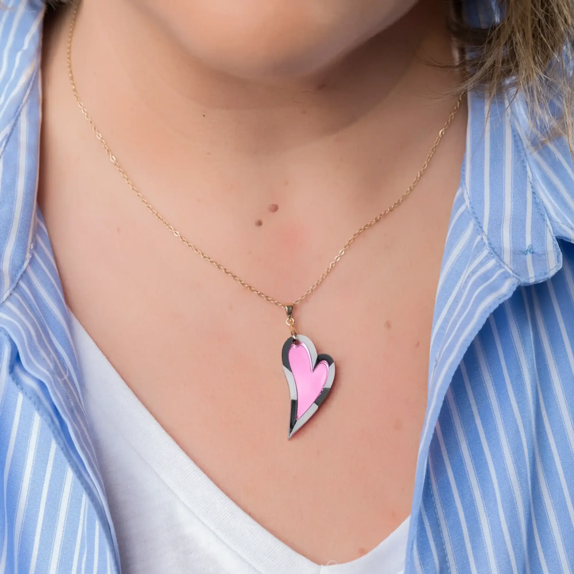 Modelo en plano medio luciendo el colgante Latido en forma de corazón alargado, en color fucsia, con cadena chapada en oro de 14k. También lleva los pendientes Latido en tamaño grande, creando un look vibrante y moderno.